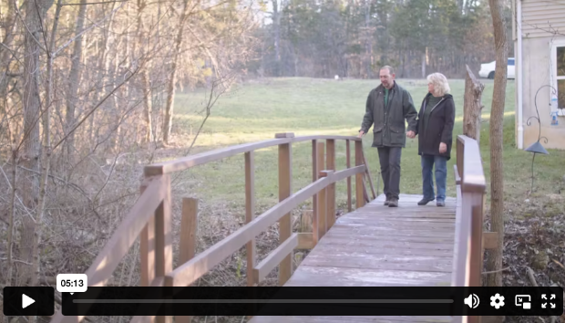 Kerry and a companion walking hand in hand across a wooden bridge outside their home, Somatuline® Depot patient story.