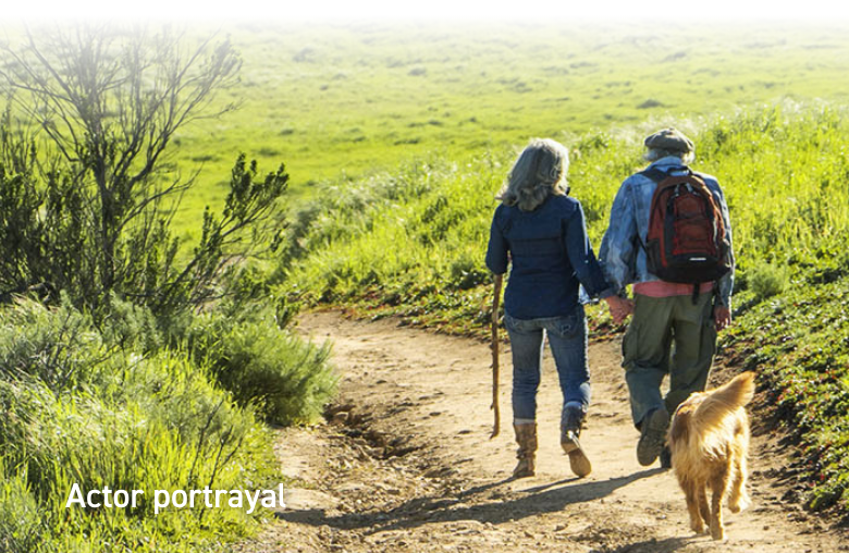 Image of a woman and a man walking their dog down a path